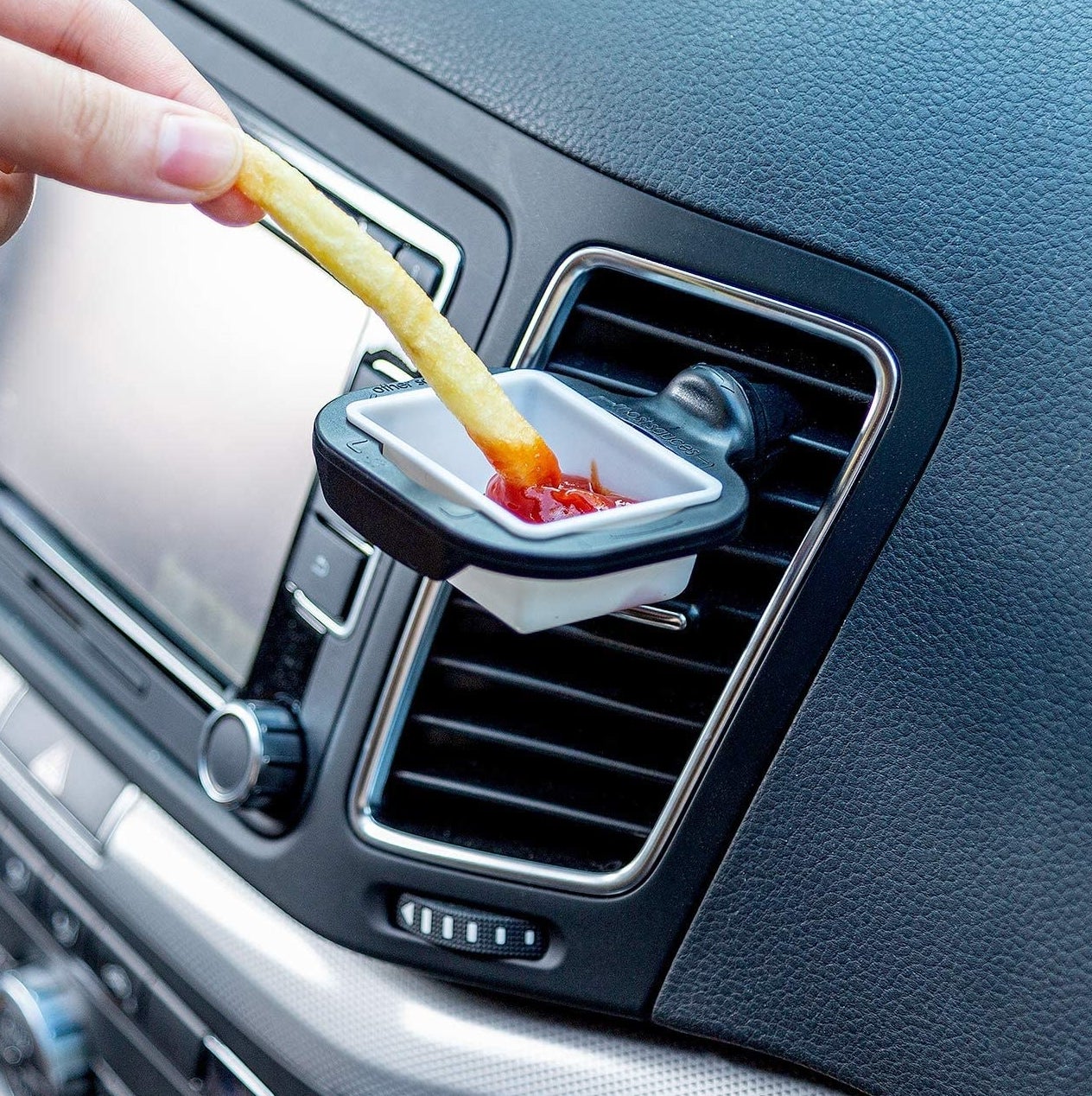 A person dipping a french fry into ketchup being held up by the holder in a car