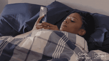 A GIF of someone sitting in bed staring at their phone