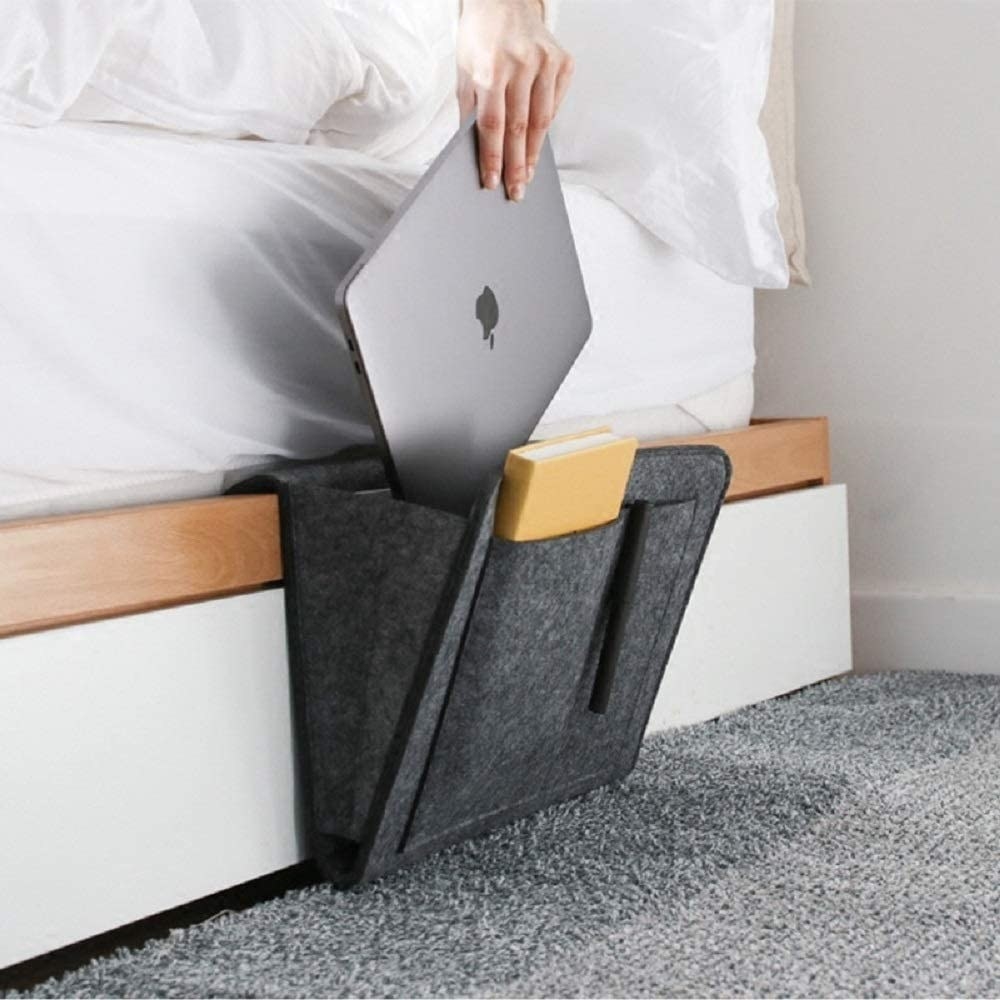 a person placing a laptop into a bedside caddy that is hanging over a bed frame