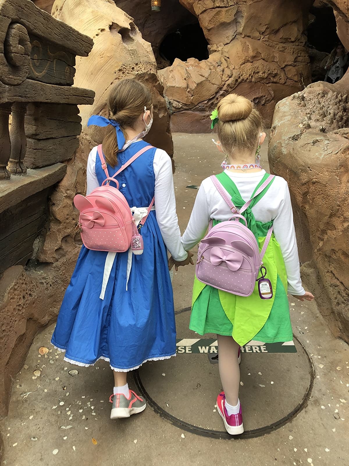 reviewer's photo of their children carrying the pink and purple mini backpacks at Disney
