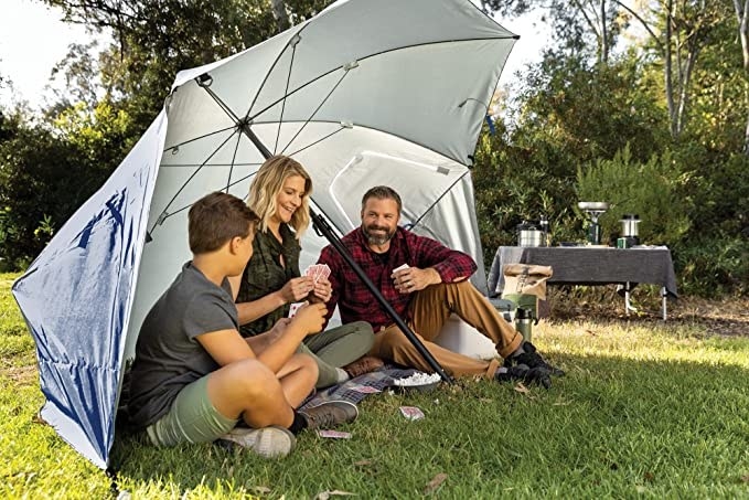 a family sitting under the large sports umbrella mounted into the ground