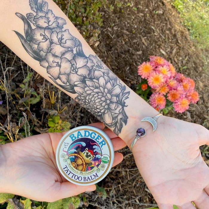 A person holding the tattoo balm in one hand while showing off their forearm sleeve