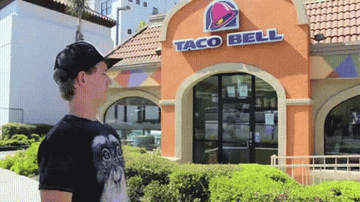 Guy wearing a baseball cap pumps his fist in front of a Taco Bell