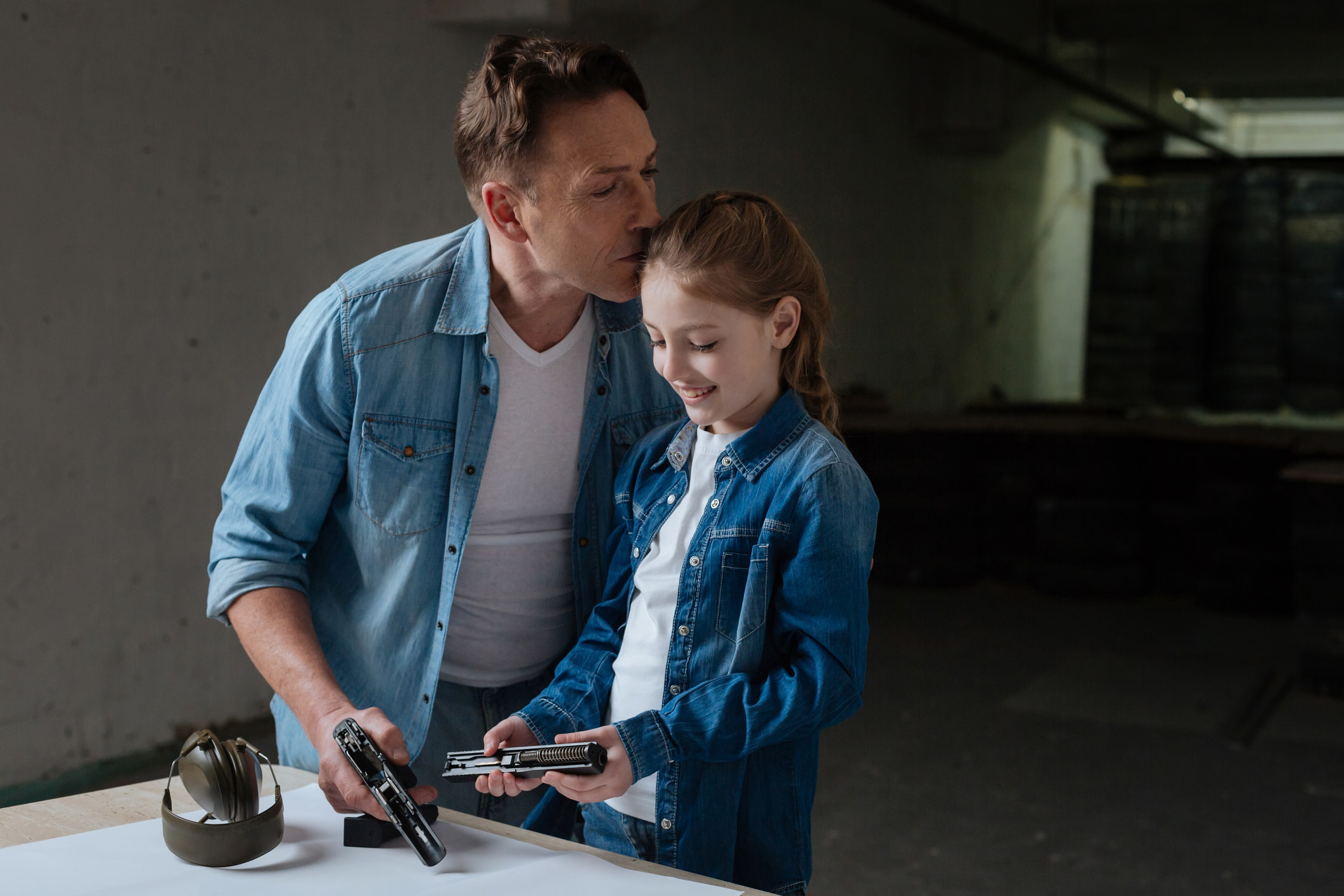 a dad kissing his daughter&#x27;s forehead while they get ready to shot guns