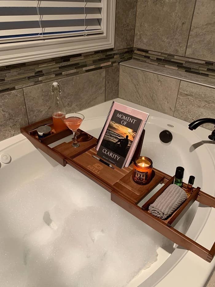bubbly bath tub below wood tub caddy with a book, lit candle, and glass of wine