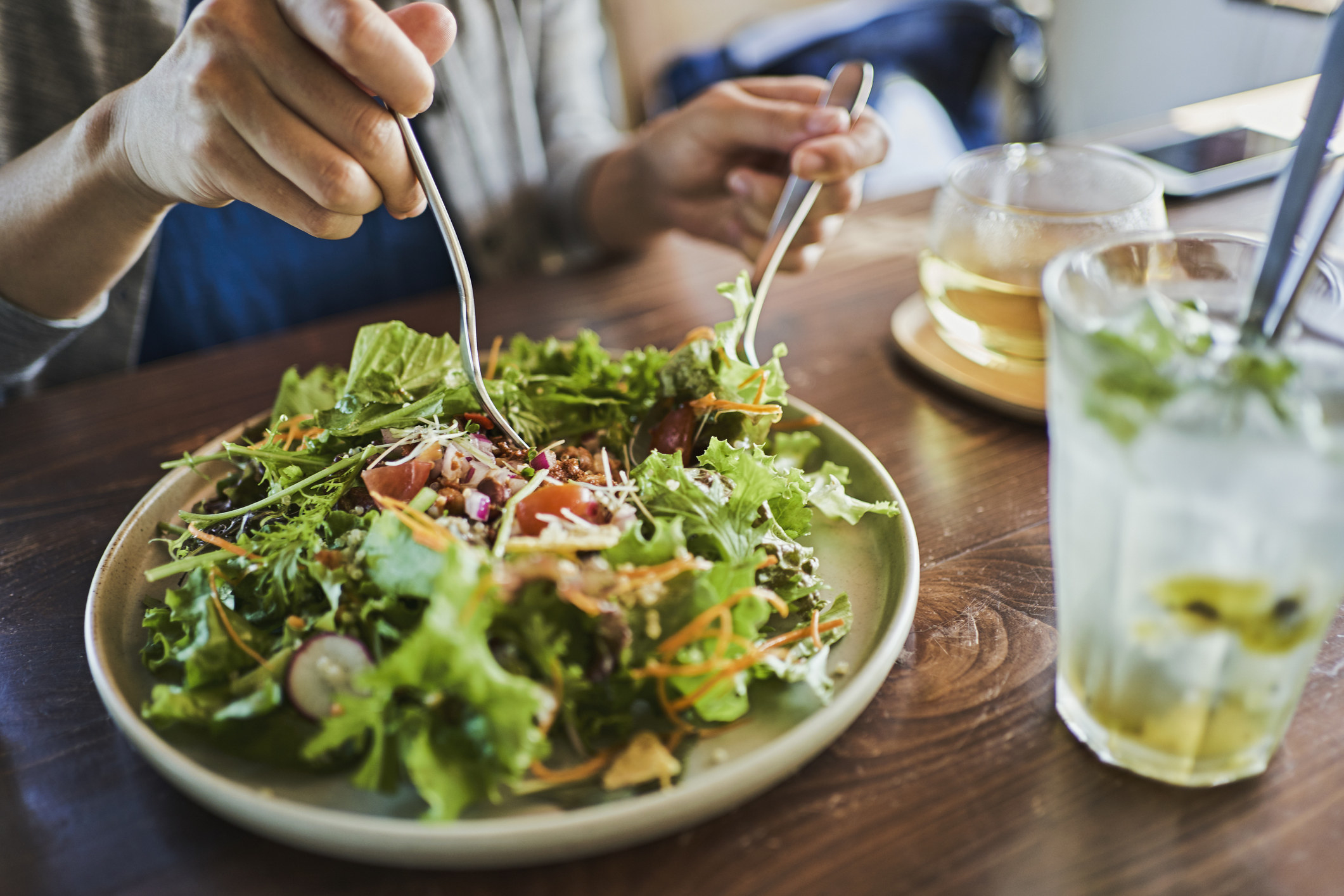 A person tossing their salad on a plate.