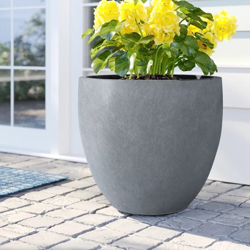 gray planter on patio with yellow flowers in it