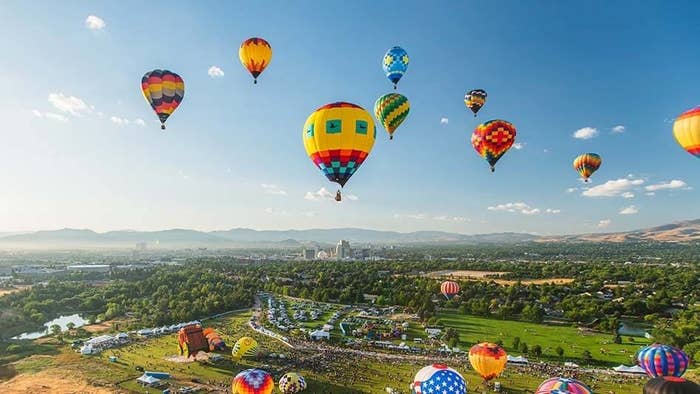 a group of hot air balloons flying over Reno hills