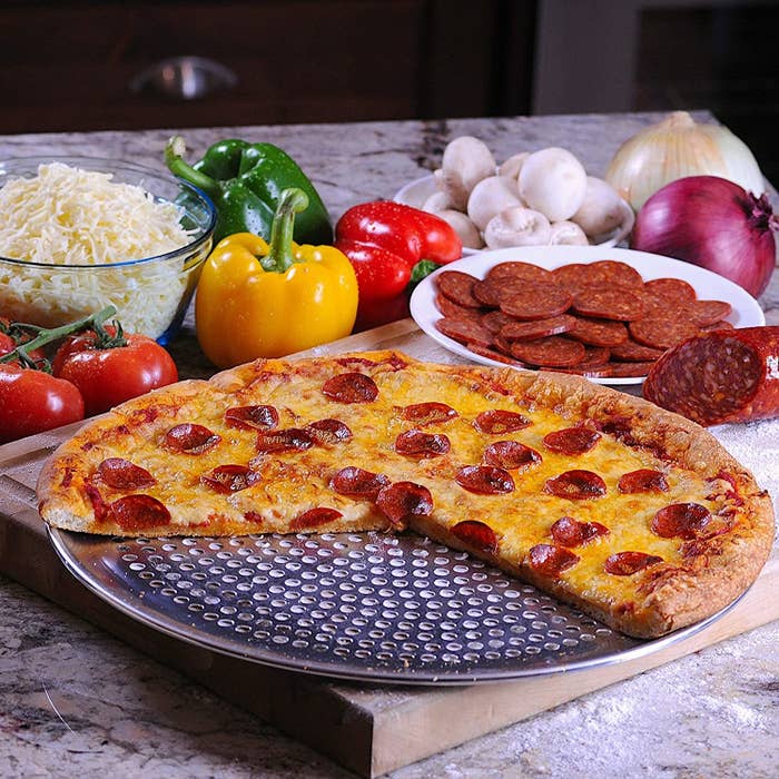 A pizza on the pan surrounded by ingredients