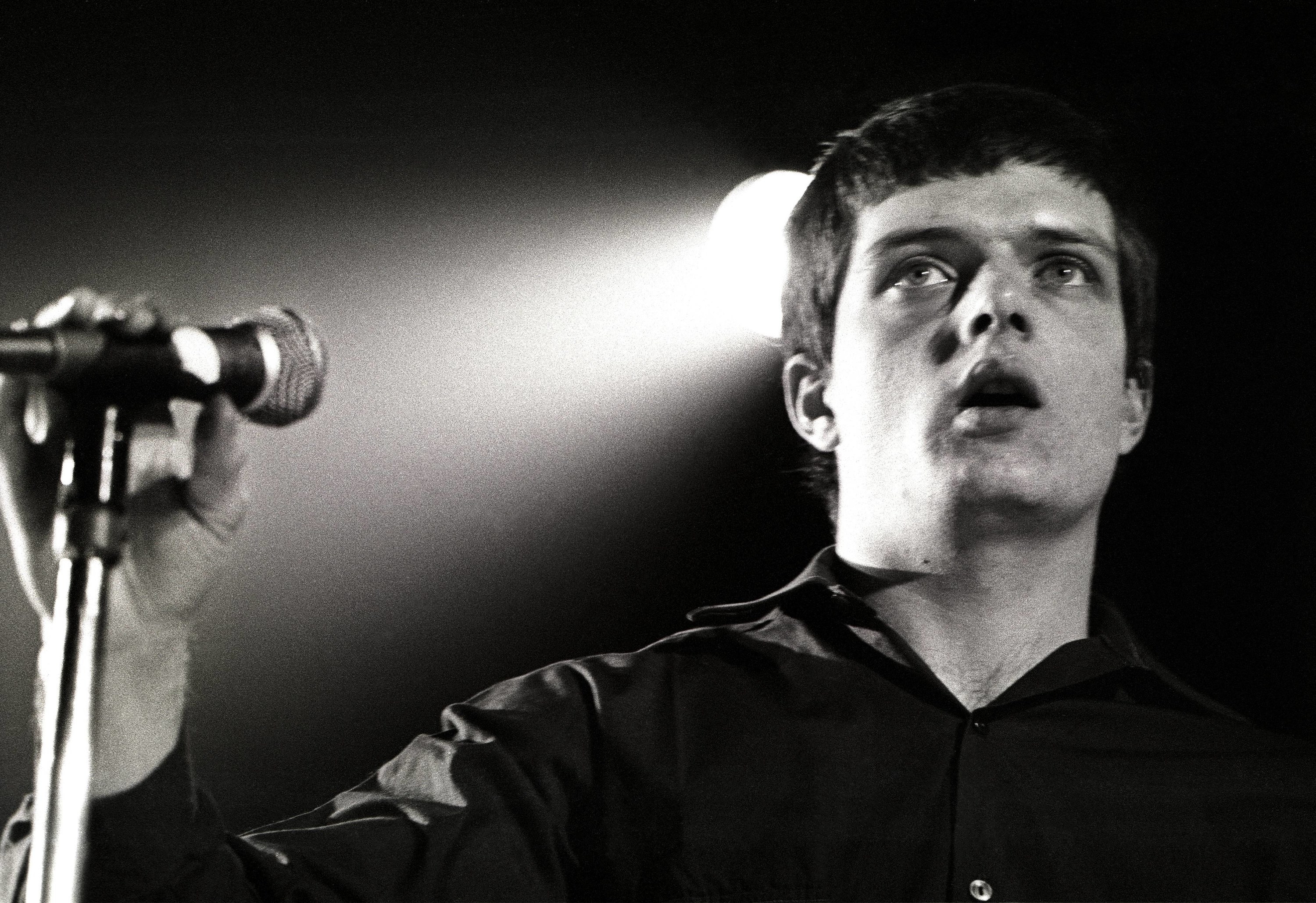 Ian Curtis standing by a mic