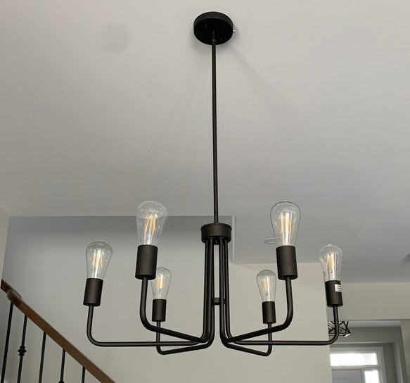 The black, six-light fixture hangs in a dining room