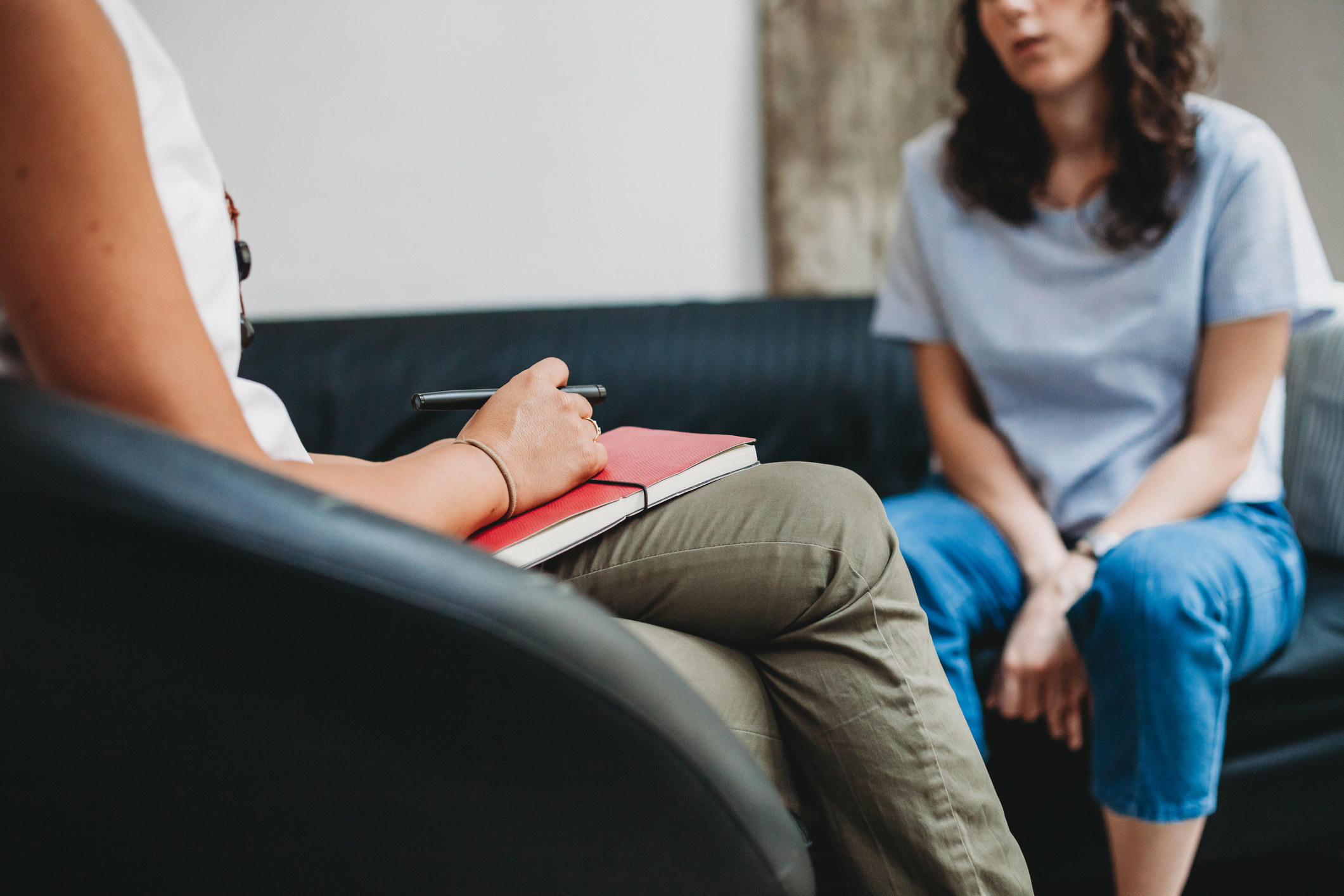 A woman sits on a couch and speaks to a therapist in a chair