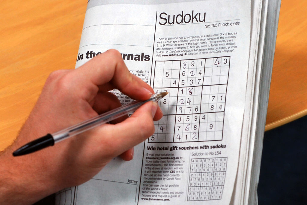 someone filling out a Sudoku puzzle in the newspaper
