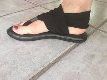 reviewer photo of side view of black flat sandals with a sling wrap around the ankles