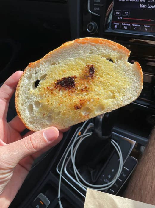 A hand holding a piece of Vegemite toast in a car