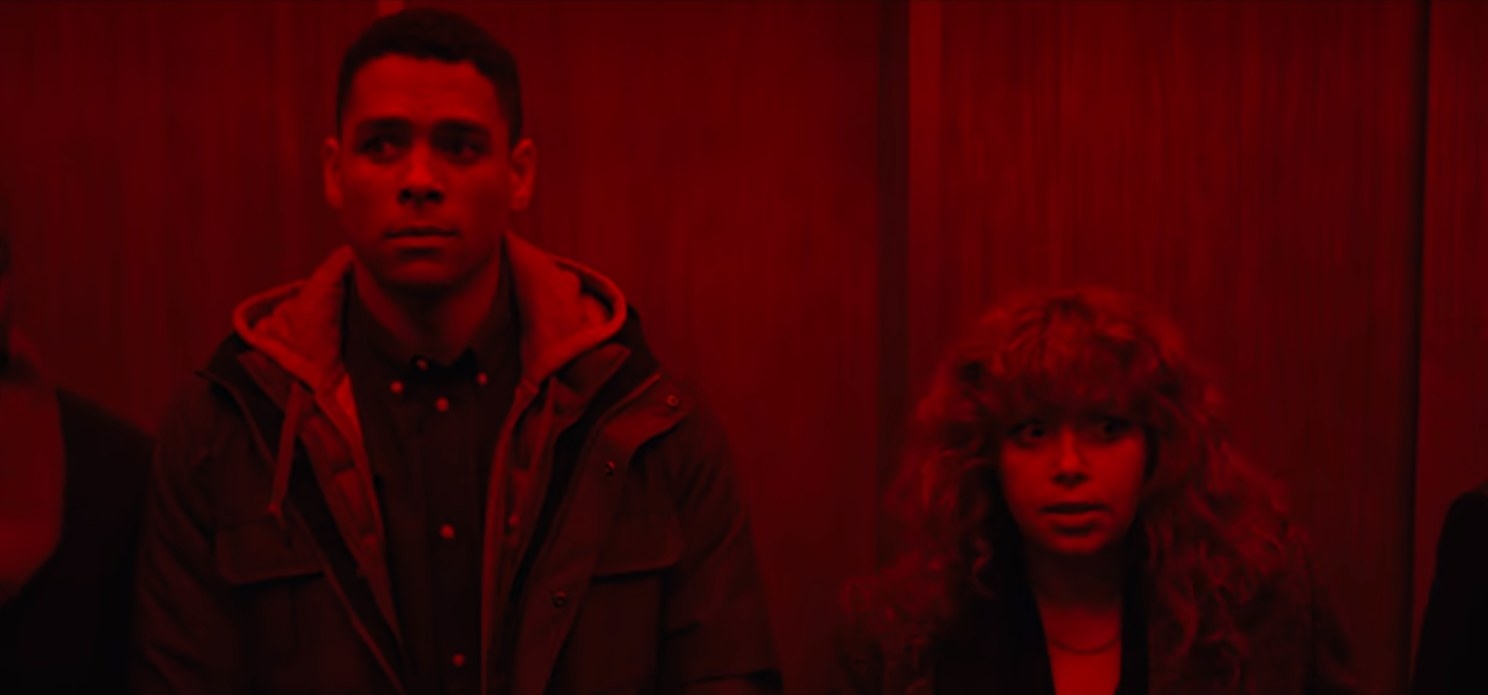 Alan and Nadia stand in the elevator under red lights