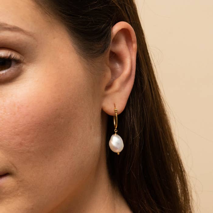 A model wearing a gold hoop earring with a large pearl on the end
