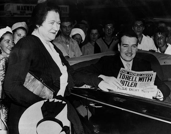 Black-and-white photo of seated man smiling and holding the Hobo News with the headline &quot;To Hell With Hitler: Public Enemy No 1&quot;