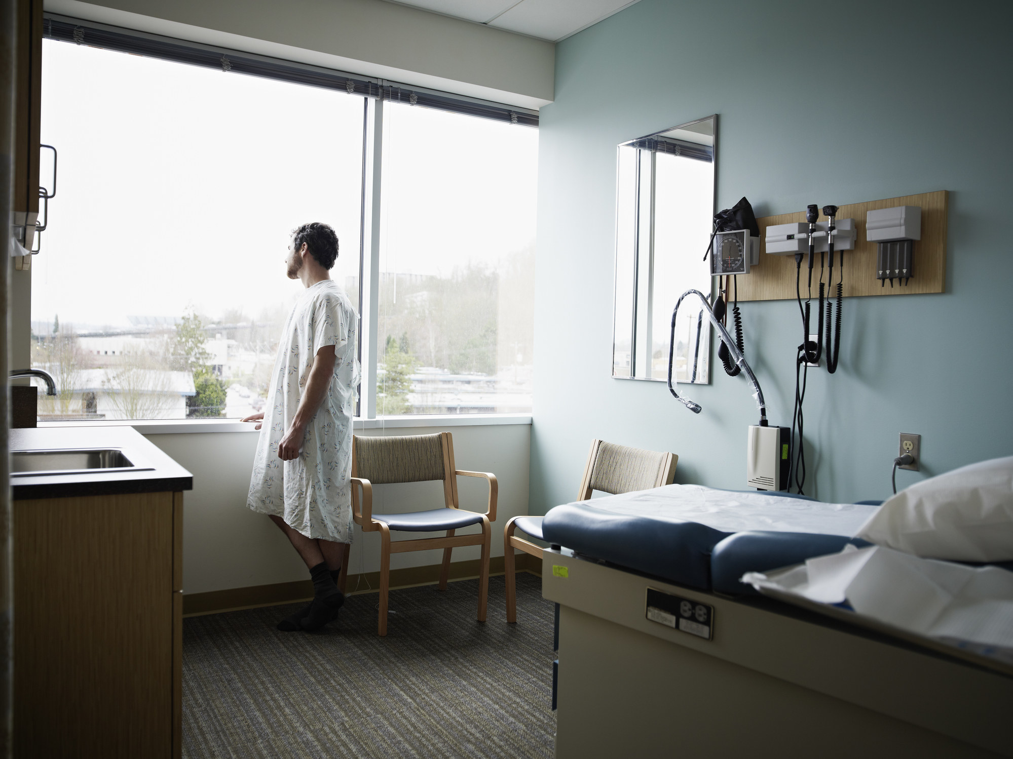 a man in a hospital gown looking out the window of the exam room