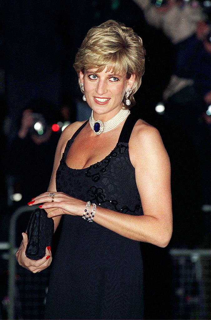 Princess Diana in a classic sleeveless black dress and holding a purse