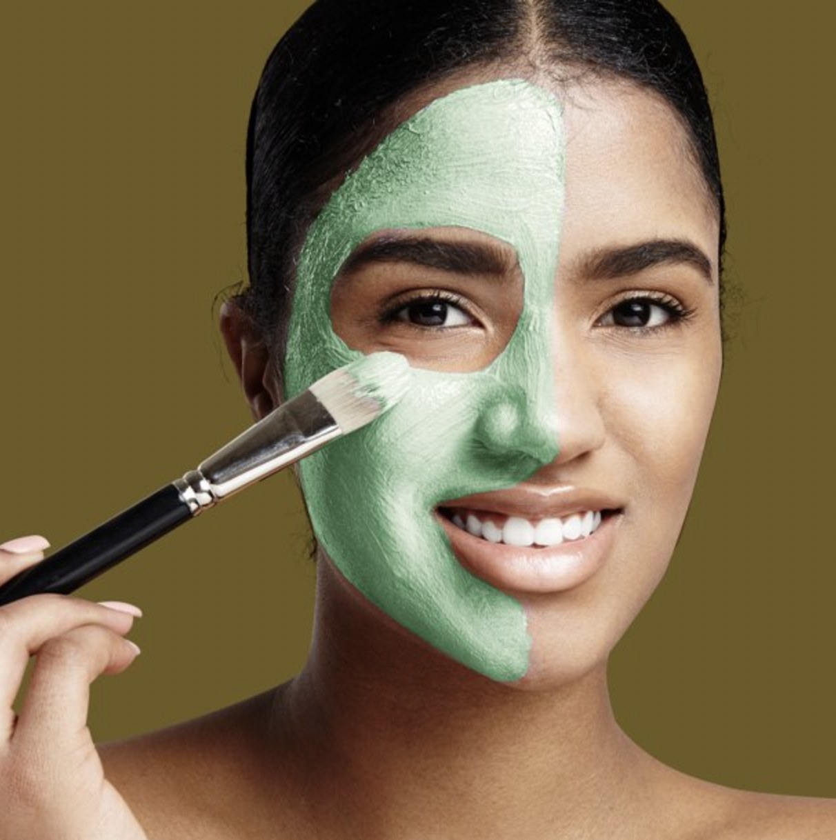 A person applying a green face mask to half of their face