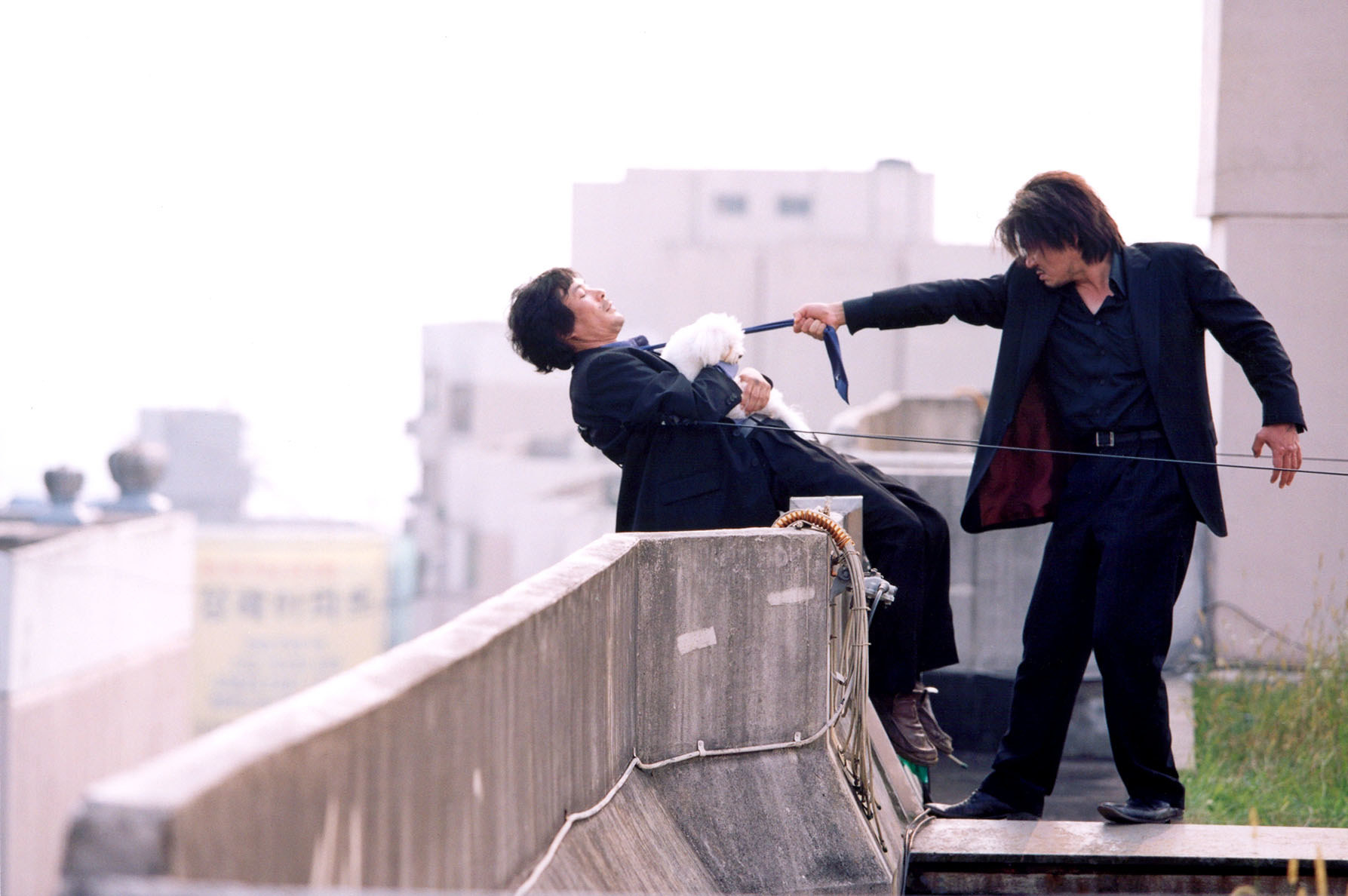 A person pointing a gun at a person on the ledge of a building