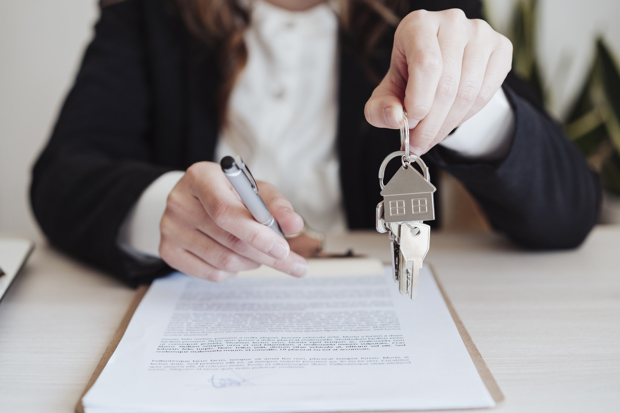 A real estate agent holding a pen some keys on a house-shaped keyring