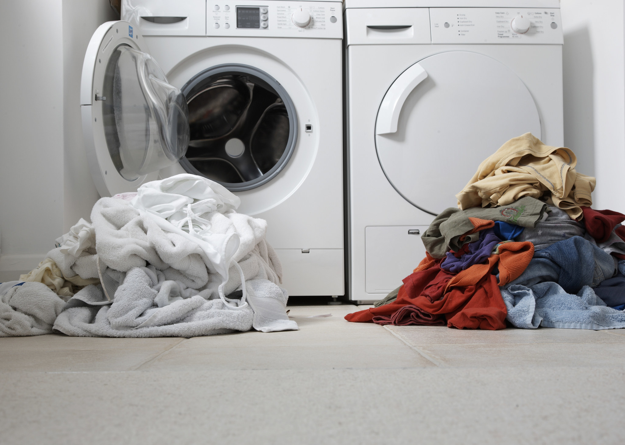 Two piles of clothes sit next to a washer and dryer