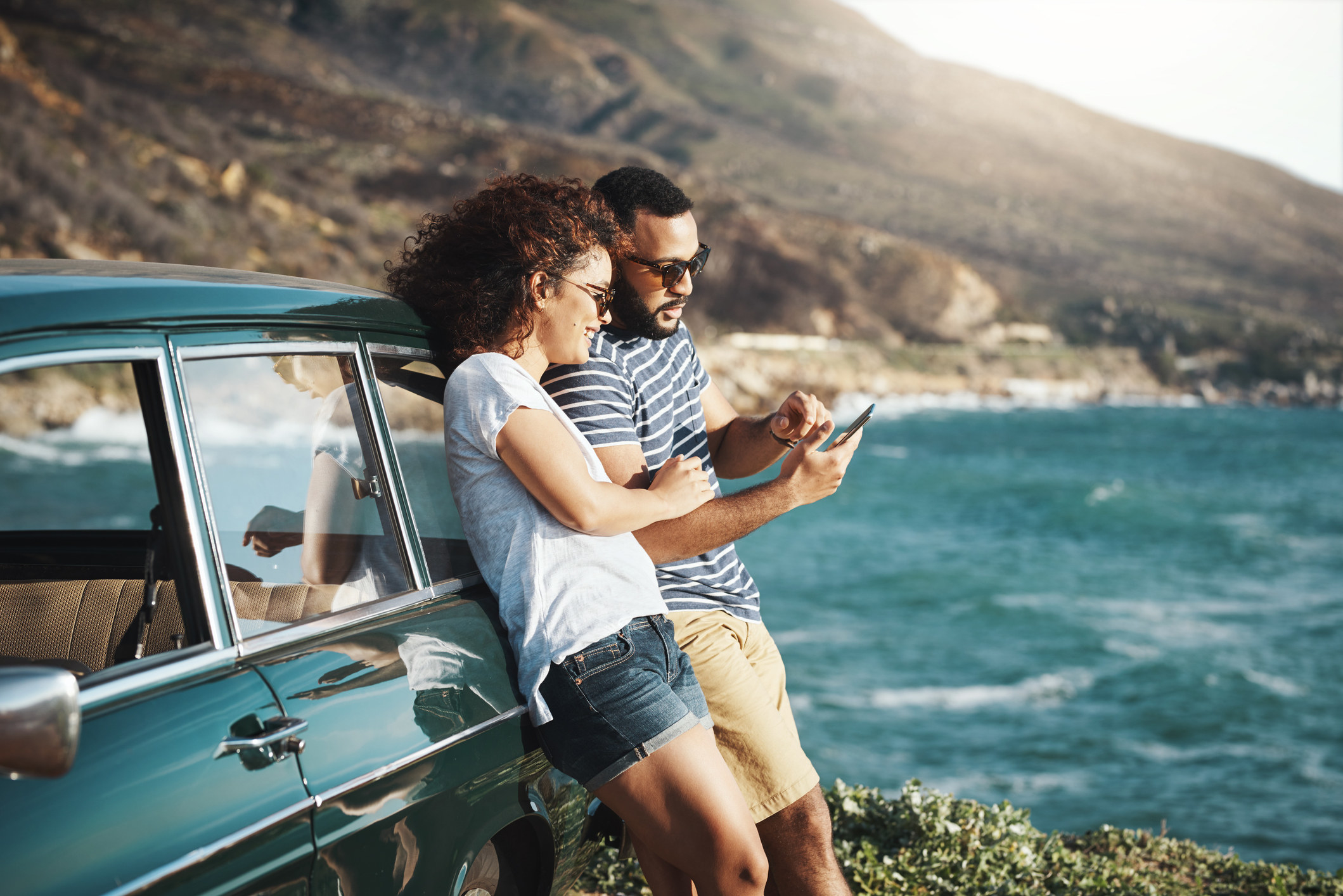A couple leans against their car as they stand beside the beach
