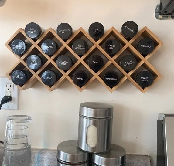 Wall-mounted wooden spice rack with various labeled spice jars, above a kitchen counter holding three metallic canisters