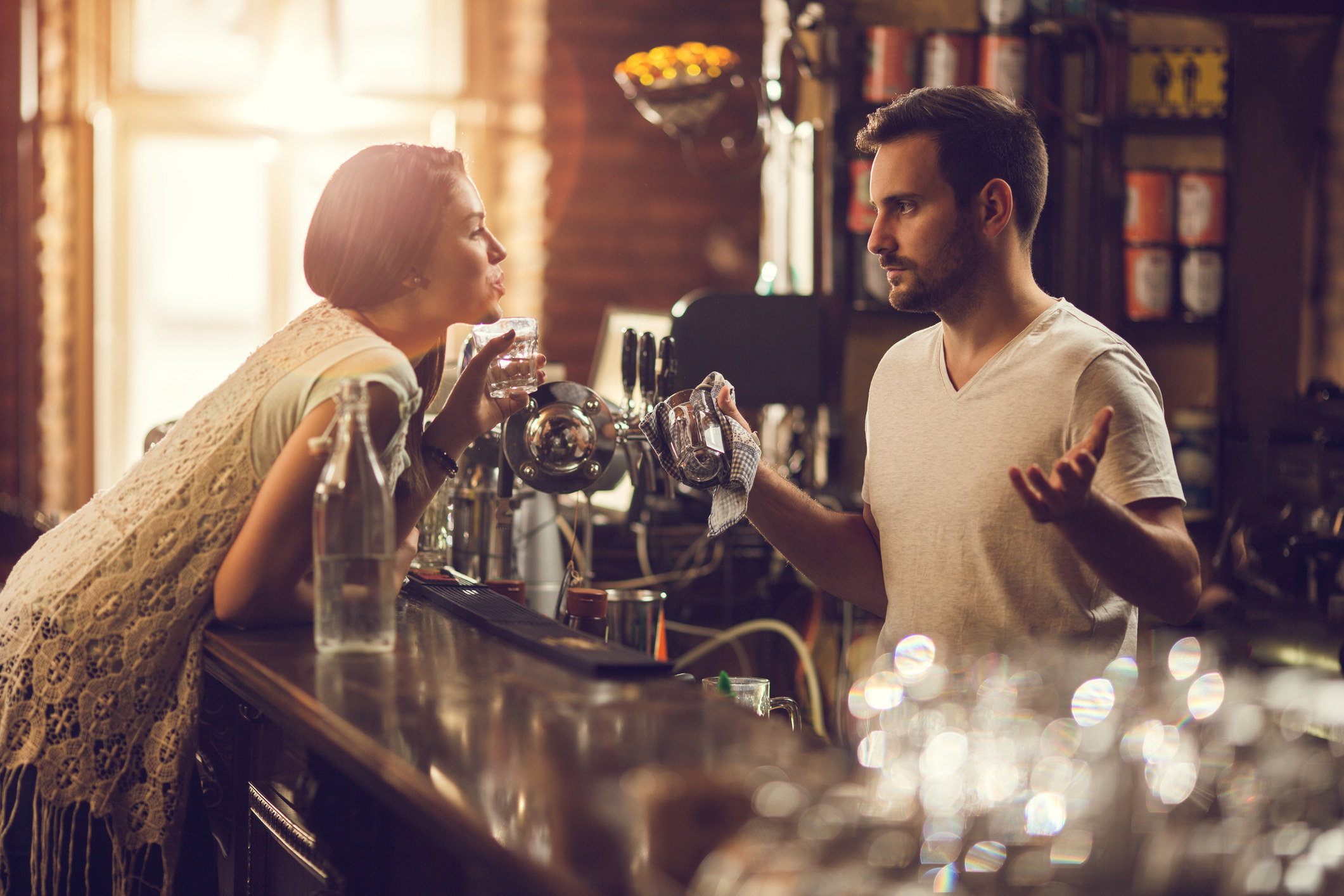A woman leaning over the bar while talking to a bartender.