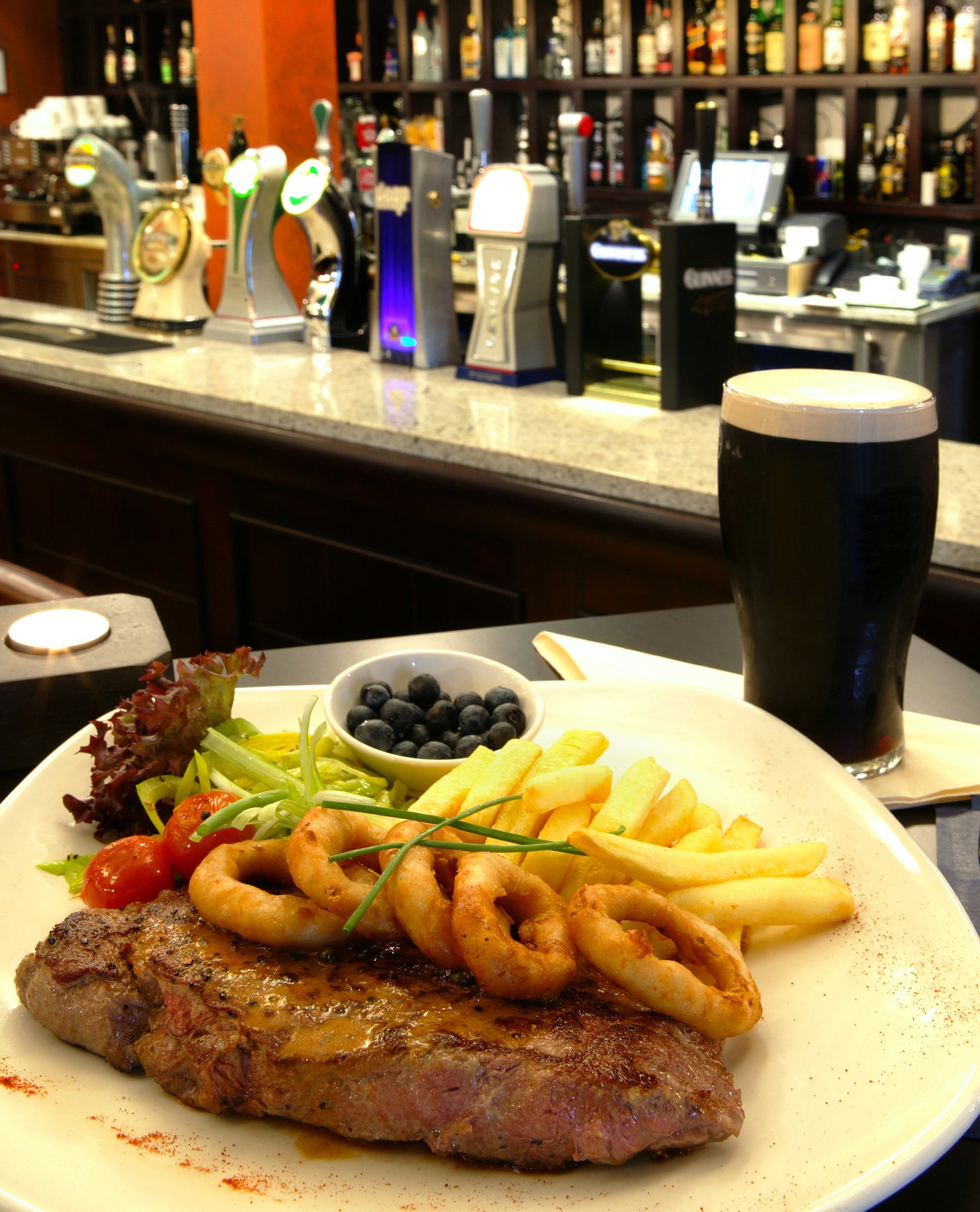 A pint of Guinness next to a steak dinner.