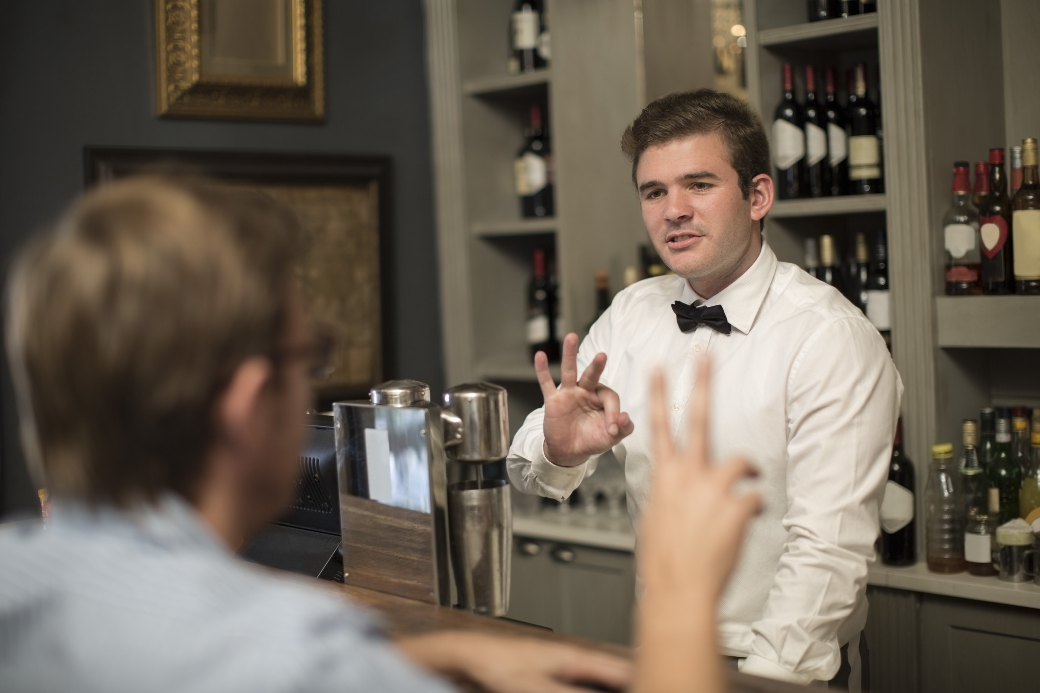A bartender giving a customer the &quot;okay&quot; symbol.