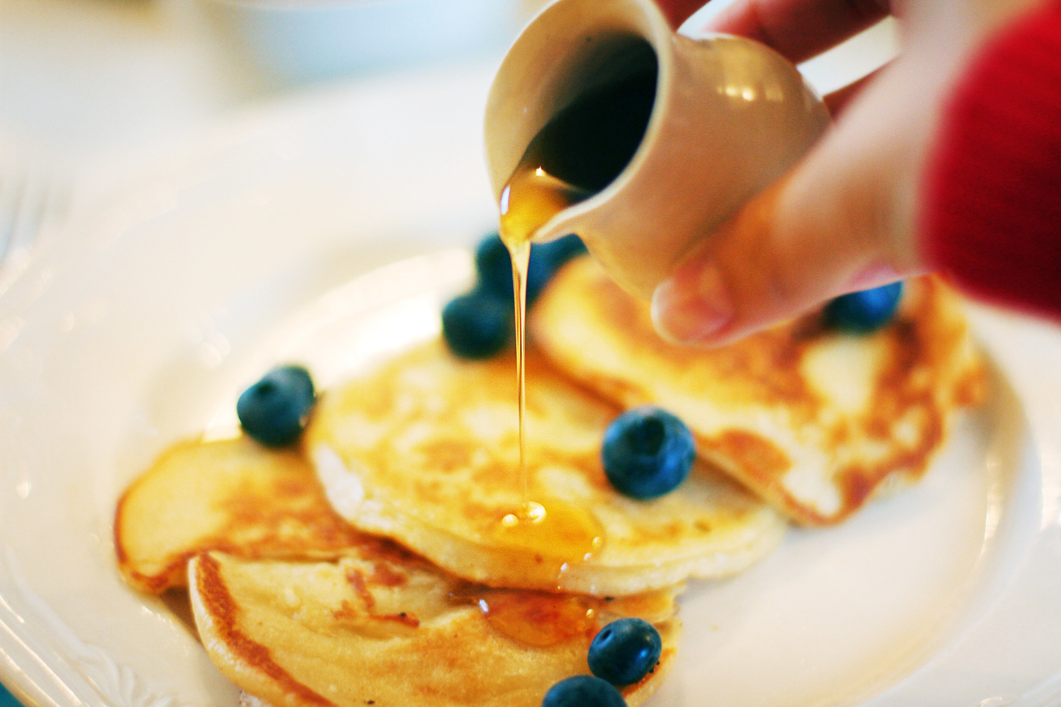Woman pouring maple syrup over thin pancakes with blueberries.