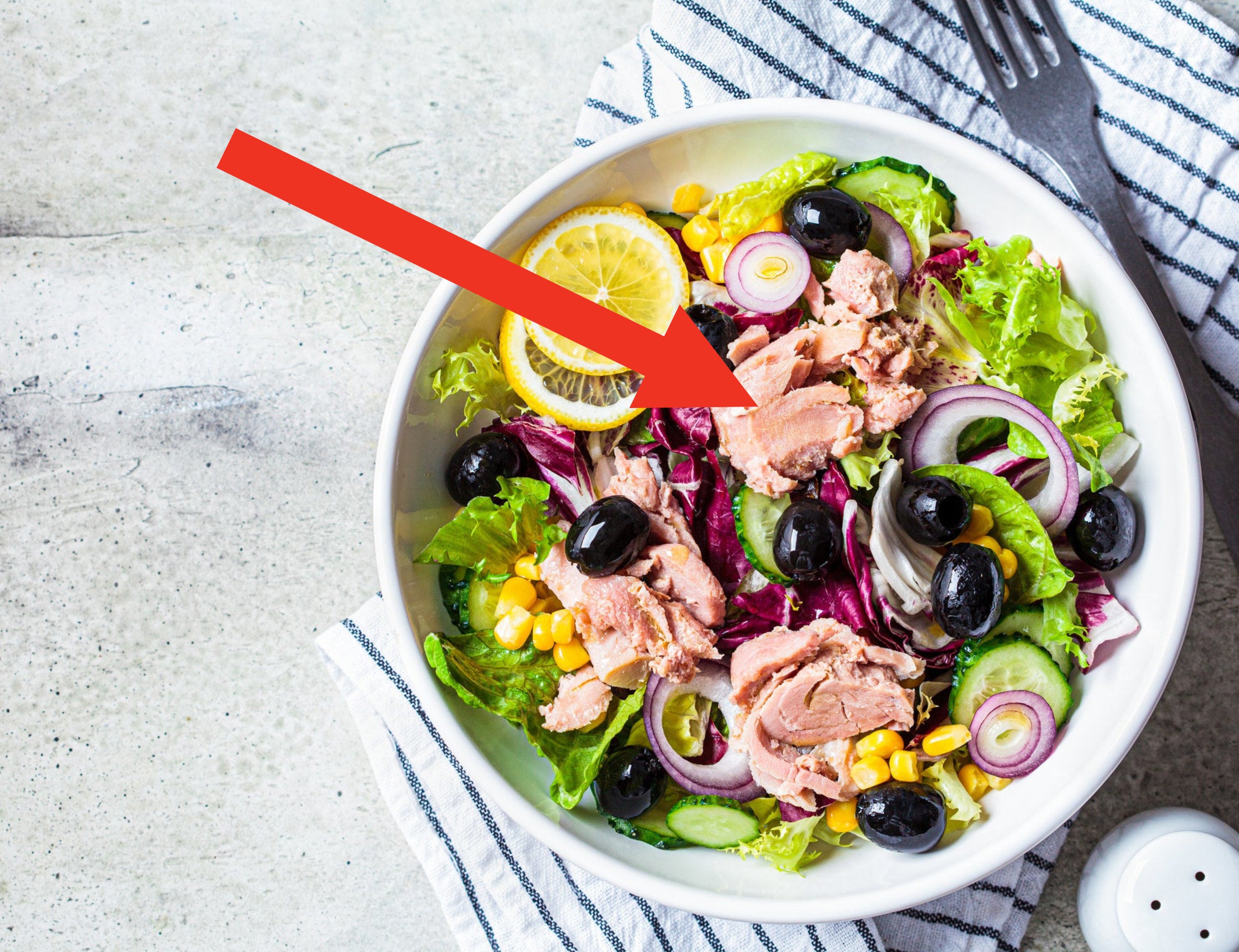 Tuna salad with cucumbers, corn, olives and red onions in a white bowl.