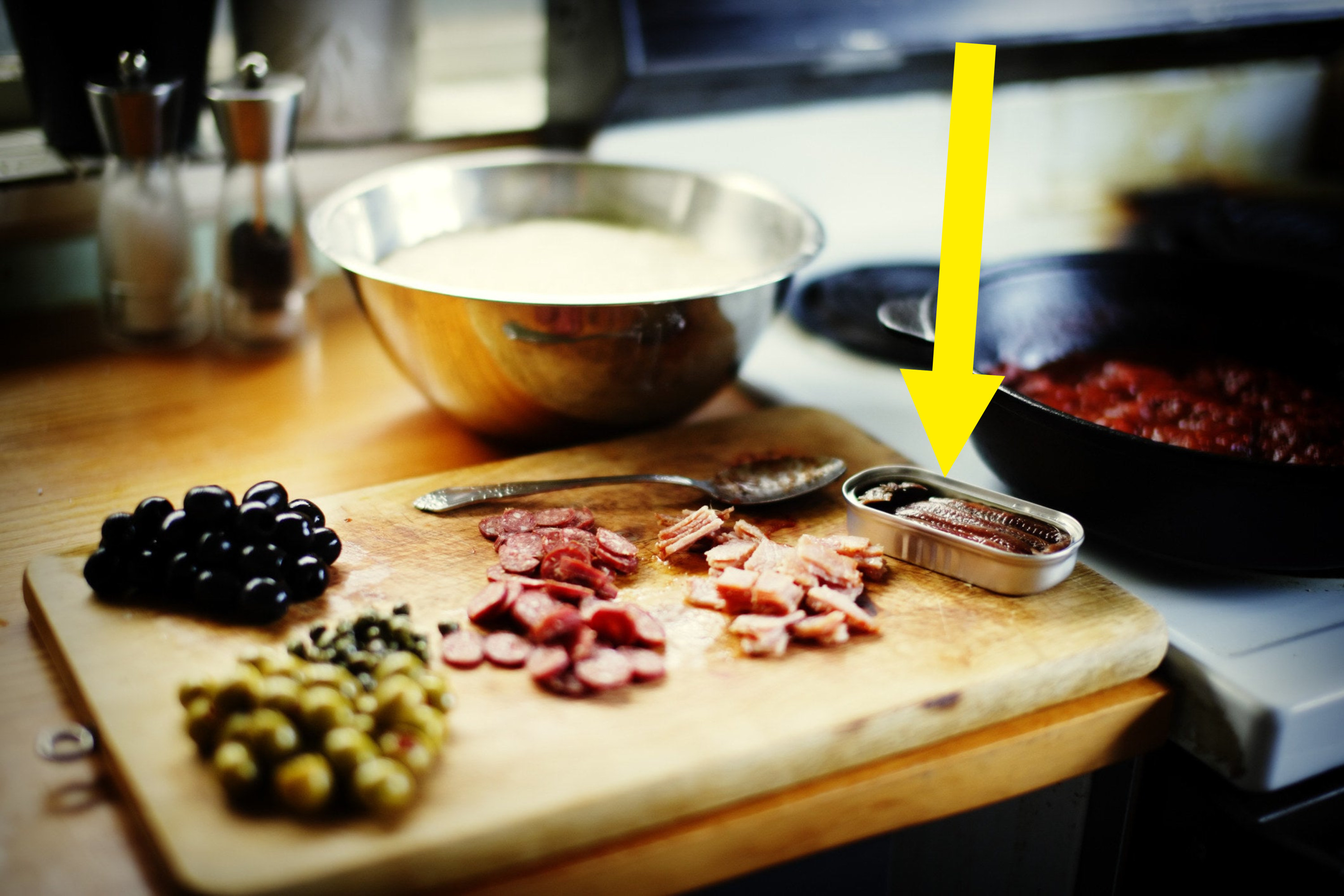 Ingredients on. a cutting board including olives, pepperoni, and anchovies.