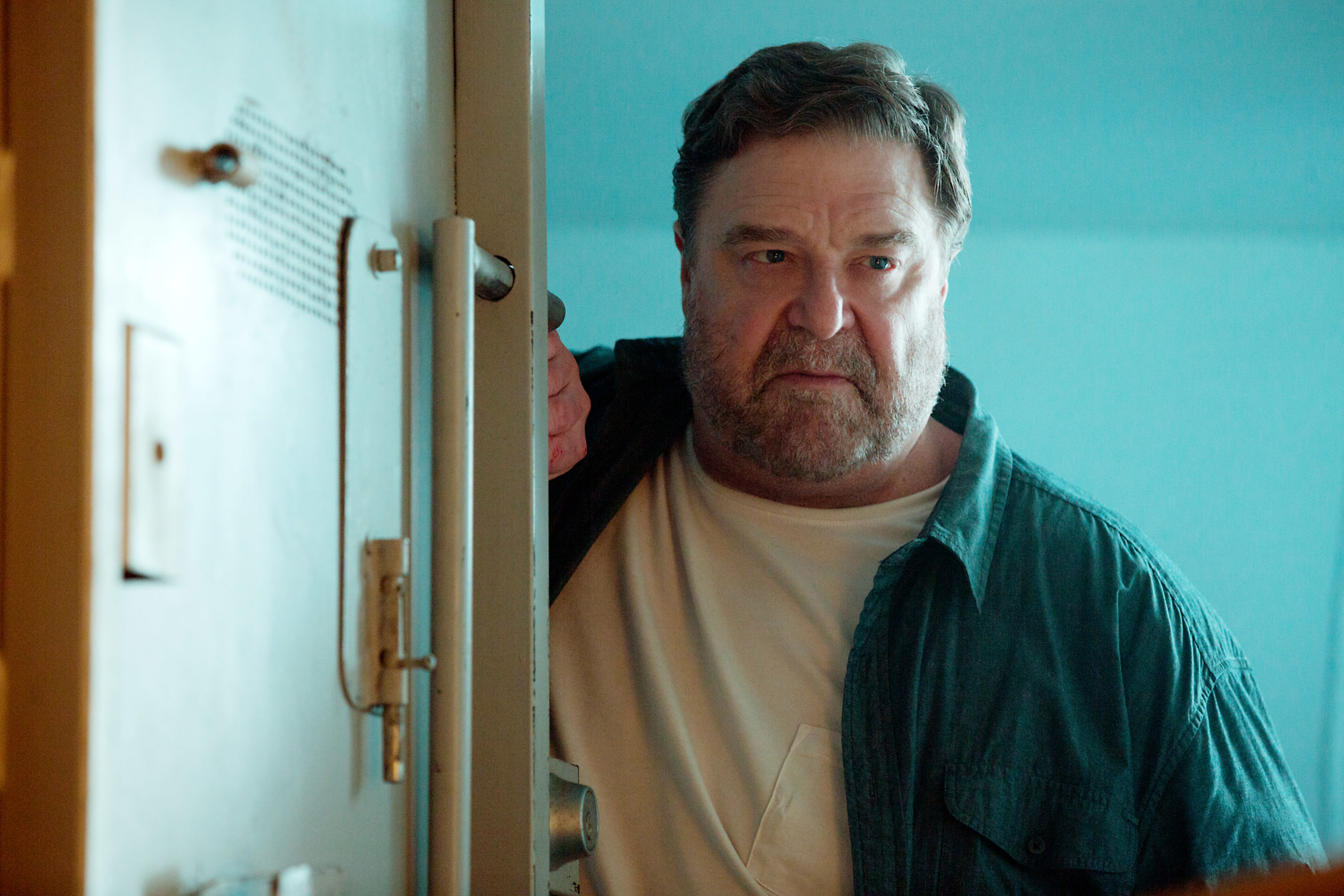 John Goodman stands against a door