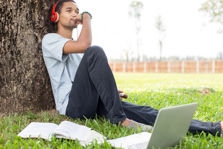 A man sitting in a park and listening to music on his headphones.