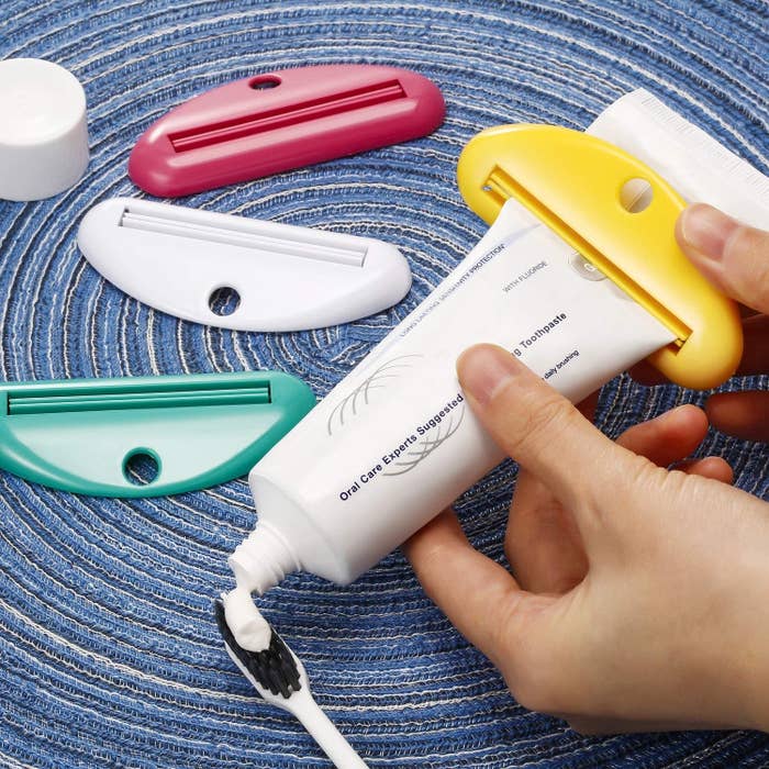 a person using the squeezer to apply toothpaste to a toothbrush