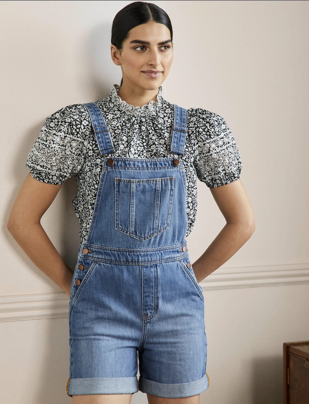 Model wearing the light blue denim short overalls over a puff sleeve black and white patterned blouse
