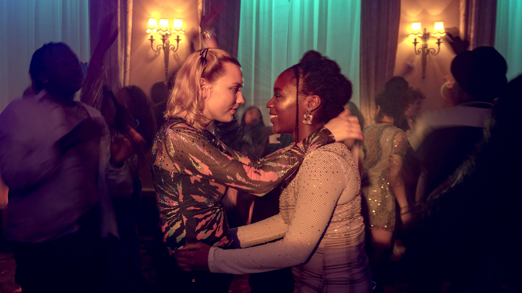 A still from Heartstopper shows two girls Tara and Darcy slow dancing together at a party and smiling