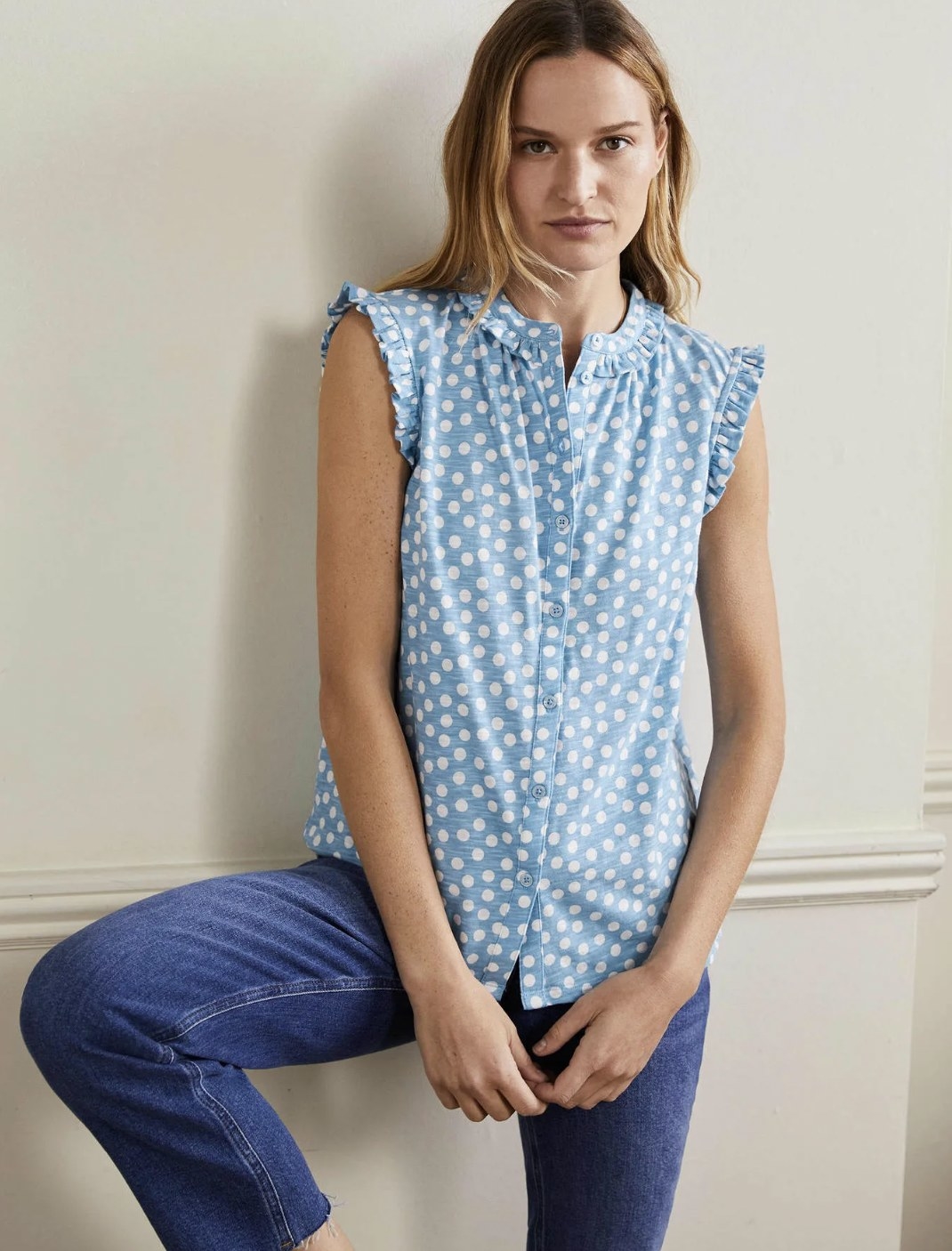 Model wearing the blue with white polka dots tank untucked over jeans