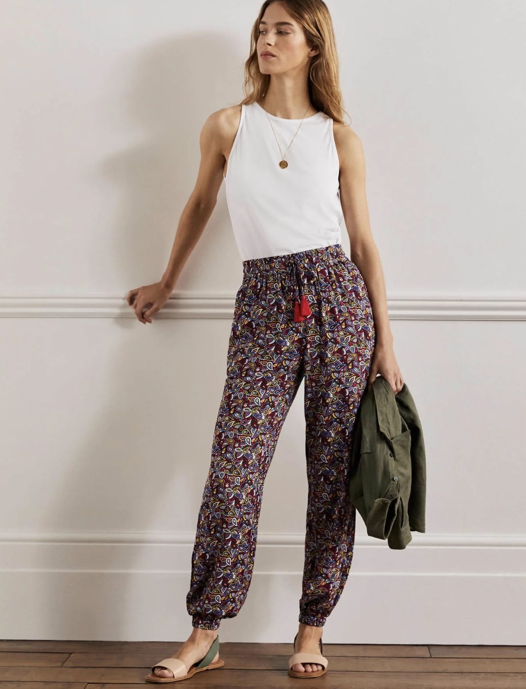 Model posing in the deep purple and red paisley pants with sandals and white tank top