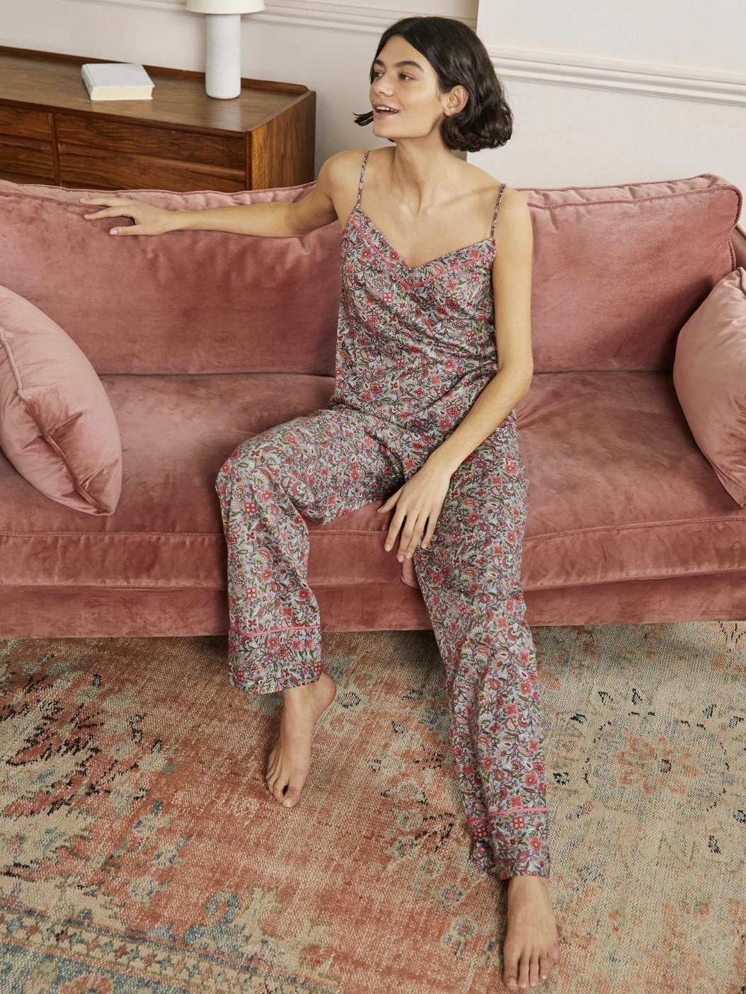 Model sitting on couch in the red and brown paisley pajama pants with matching pajama tank