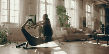 A woman in her living room rowing on a Hydrow rowing machine