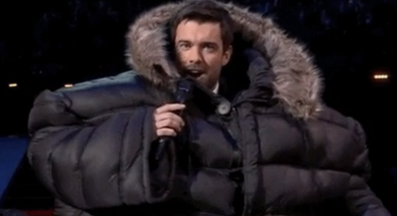 A guy speaking into a mic and wearing a huge puffy coat