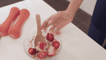 A woman shows her breakfast of cereal and berries to camera, as if filming a selfie video