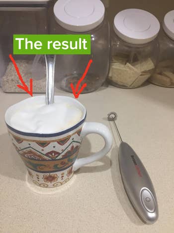Reviewer image of product in silver next to cup of coffee with foamy milk 