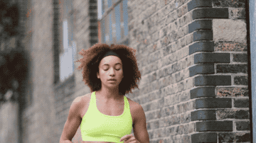 A jogging woman stops to check her fitness tracker on her wrist, then continues running