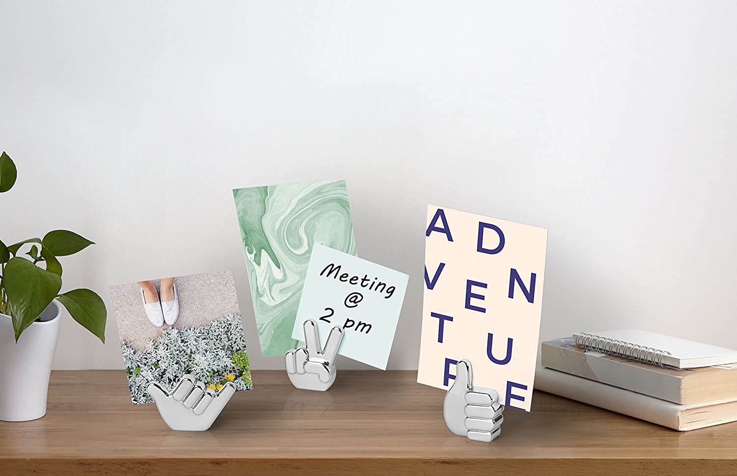 three hand shaped photo stands holding prints and notes on a desk